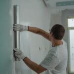Mężczyzna w białej koszuli mierzy ścianę metalową poziomicą