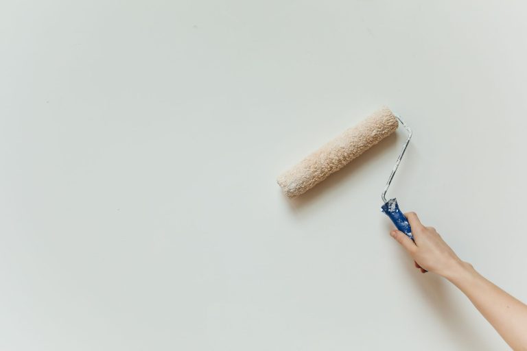 Dłoń malująca ścianę wałkiem podczas remontu