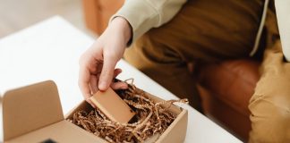 Osoba rozpakowuje mały przedmiot z kartonowej paczki wypełnionej papierem